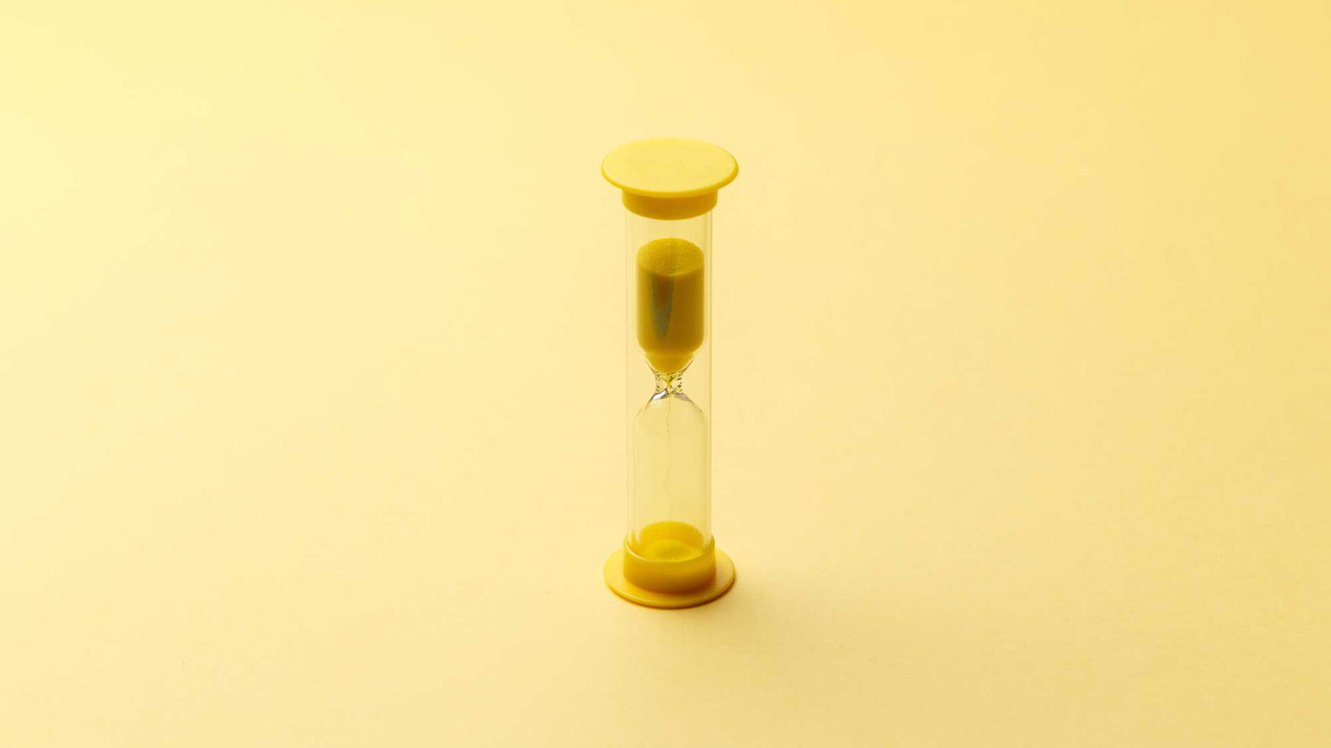Eine gelbe Sanduhr steht auf hellem Untergrund.